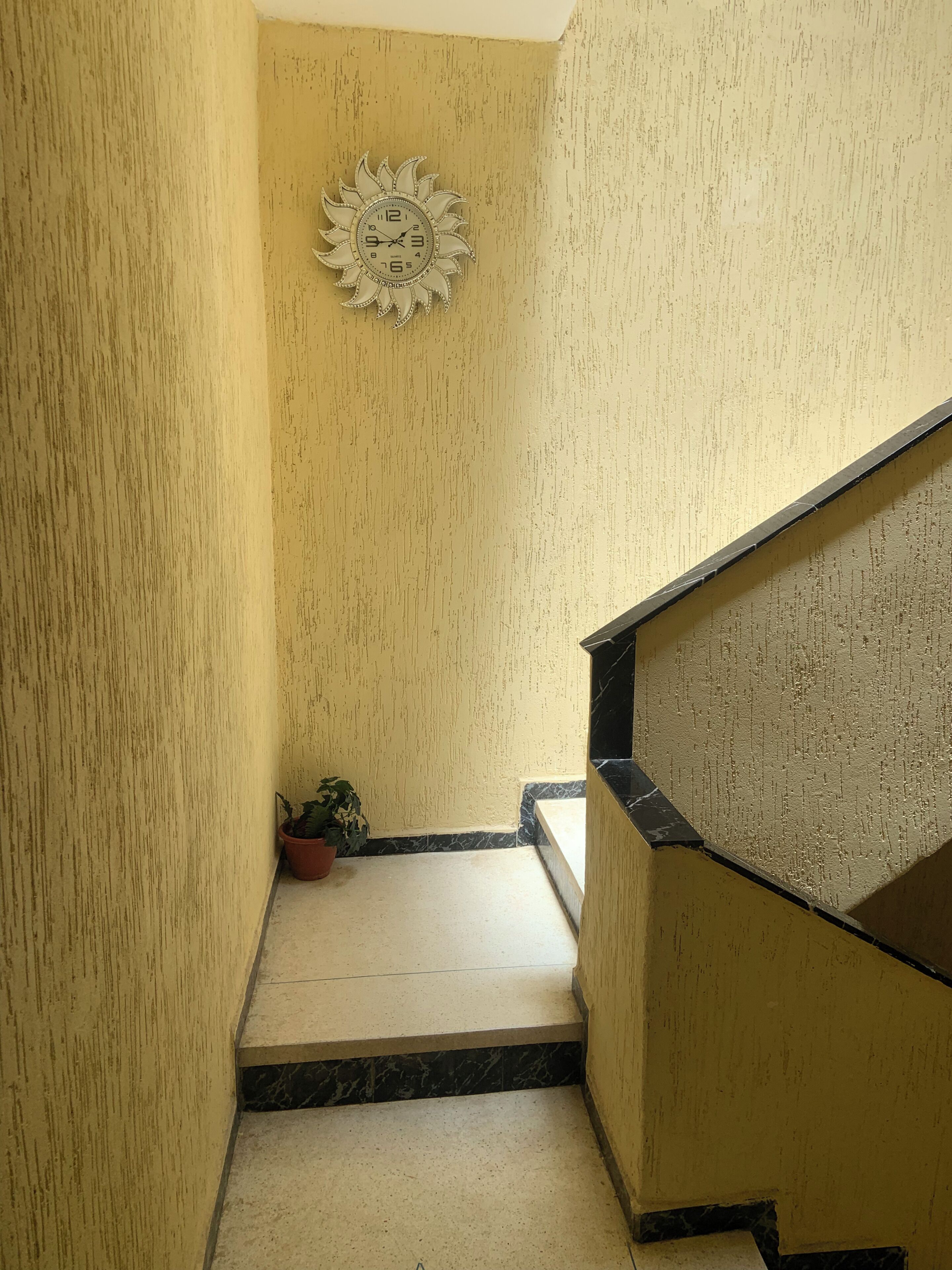 A staircase with a marble floor, a potted plant, and a decorative sun-shaped clock on the wall.