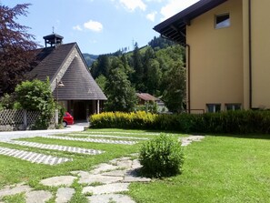 Ein Gebäude mit schrägem Dach, einem kleinen Glockenturm und einem gepflasterten Eingang, vor dem ein rotes Auto geparkt ist.