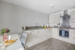 A modern kitchen with white cabinets, a stainless steel range hood, a built-in oven, and a granite countertop.