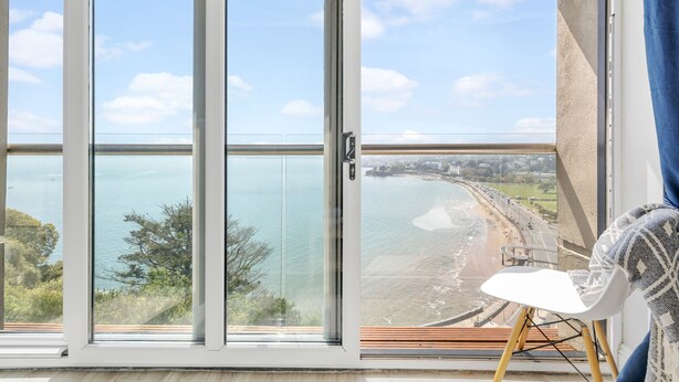 Et værelse med en stor skydedør, der fører ud til en balkon med udsigt over strand og hav.