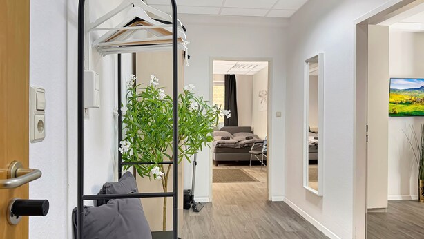 A modern hotel room with a bed, a small desk, a plant, and a view of the living area.