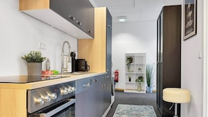 Una cocina compacta con electrodomésticos modernos, horno integrado y un pequeño comedor con un taburete.