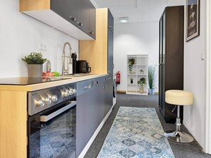 A compact kitchen with modern appliances, a built-in oven, and a small dining area with a stool. - Loft 26 Stuttgart | PS5, Darts, 12 Gäste (Stuttgart)