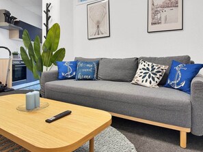 A modern living room with a grey sofa, decorative pillows, a wooden coffee table, and a remote control. - Loft 26 Stuttgart | PS5, Darts, 12 Gäste (Stuttgart)