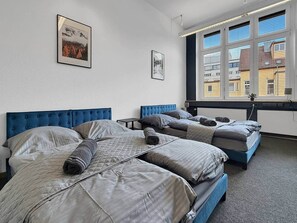 A hotel room with three beds, a window with blinds, and two framed pictures on the wall. - Loft 26 Stuttgart | PS5, Darts, 12 Gäste (Stuttgart)