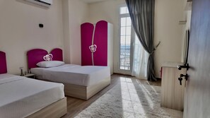 A hotel room with two beds, a large window with curtains, a wardrobe, and a radiator. - Latin District Apartments Lagoon Side (Latin District, New Alamein)