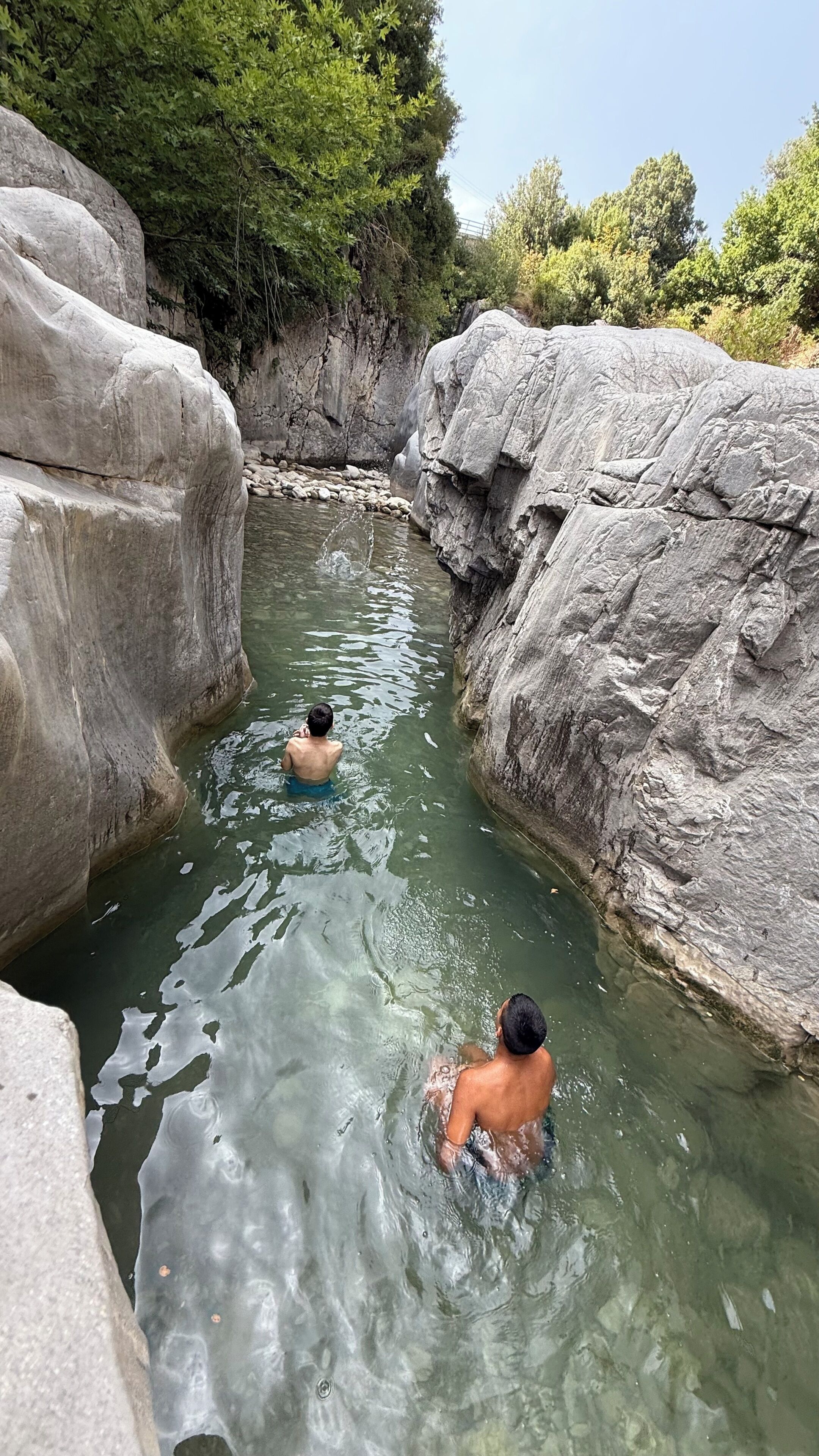 A natural pool surrounded by large rocks and trees.