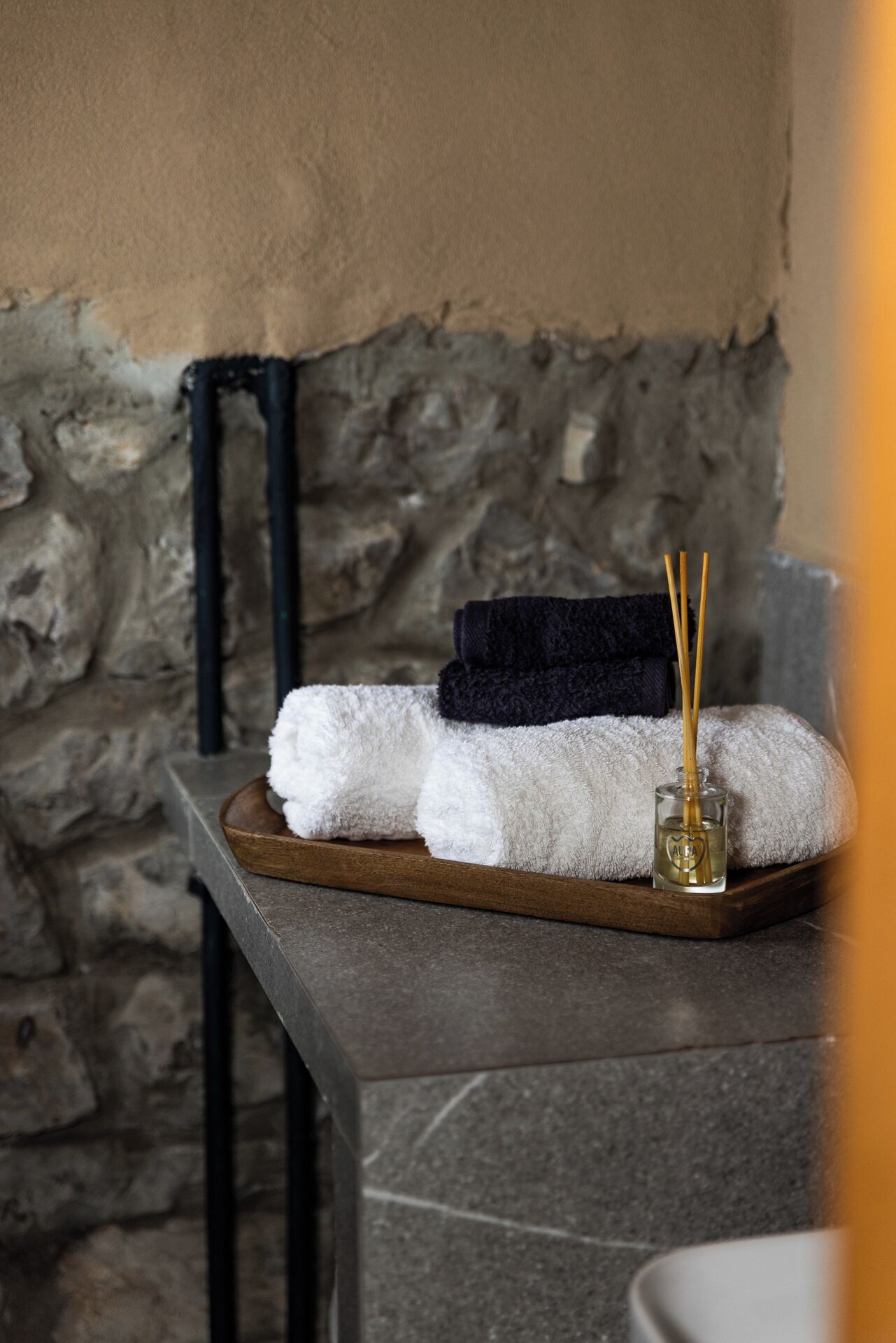 A tray with towels and a bottle of reed diffuser in a stone-walled room.