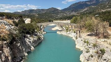 A river with a bridge, rocky banks, and distant mountains under a clear sky.