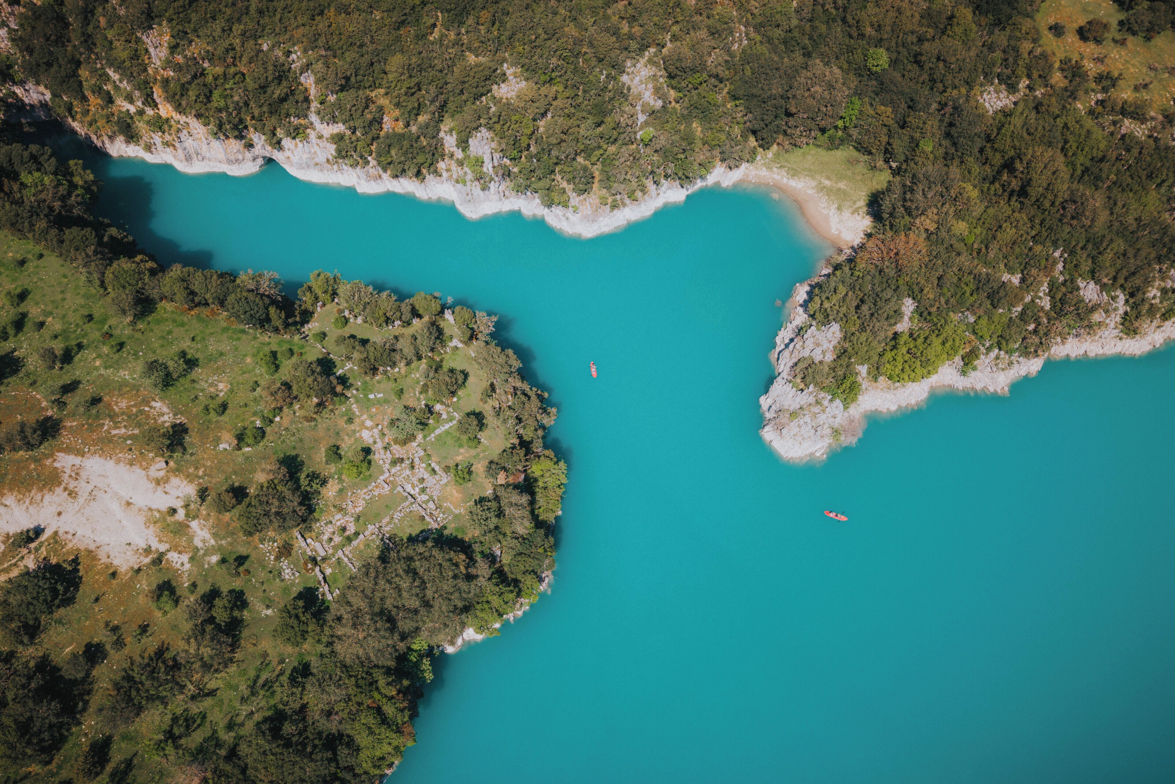 Luchtbeeld van een kustgebied met een turquoise baai, weelderige begroeiing en een klein bootje.