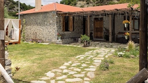 Un bâtiment rustique en pierre, avec un toit recouvert de tuiles rouges, une arche en bois portant une enseigne et un chemin de pierre menant à l’entrée.