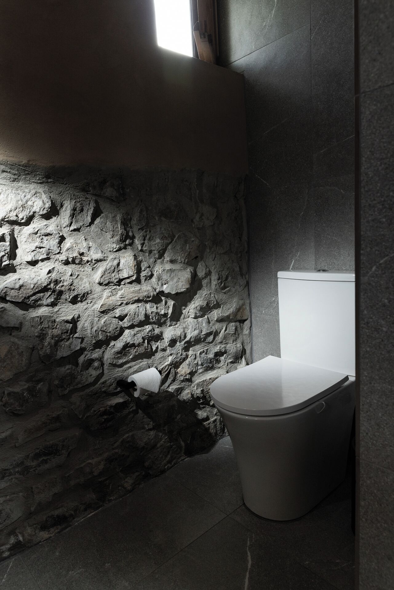 Et badeværelse med stenvæg, toilet og et vindue.