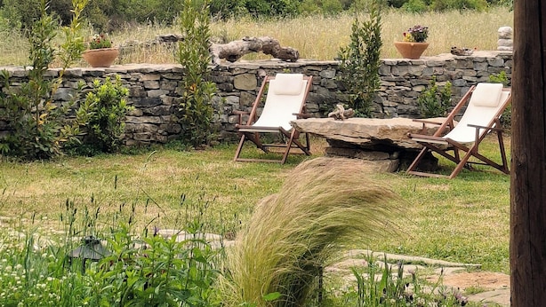 Un espace extérieur paisible, aménagé avec des murs en pierre et des fauteuils confortables, offrant une vue sur un paysage luxuriant et des montagnes lointaines.