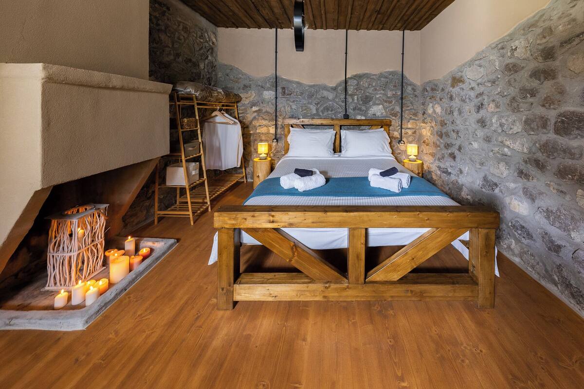 A cozy room with a wooden bed, stone walls, a hanging light fixture, and a small table with candles.
