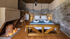 Une pièce chaleureuse avec un lit en bois, des murs en pierre, un luminaire suspendu et une petite table avec des bougies.