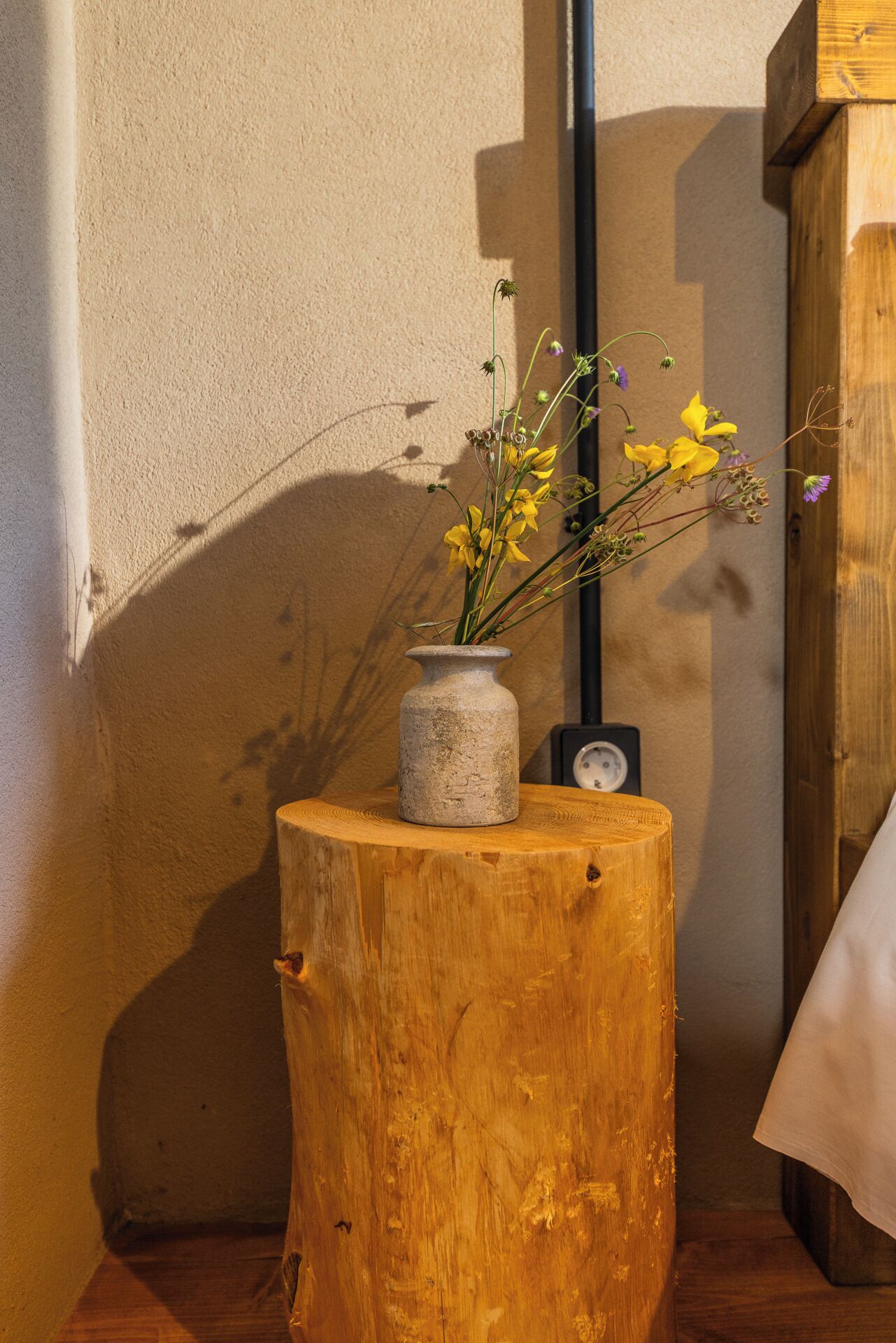 A rustic wooden stump with a vase of flowers and a clock.