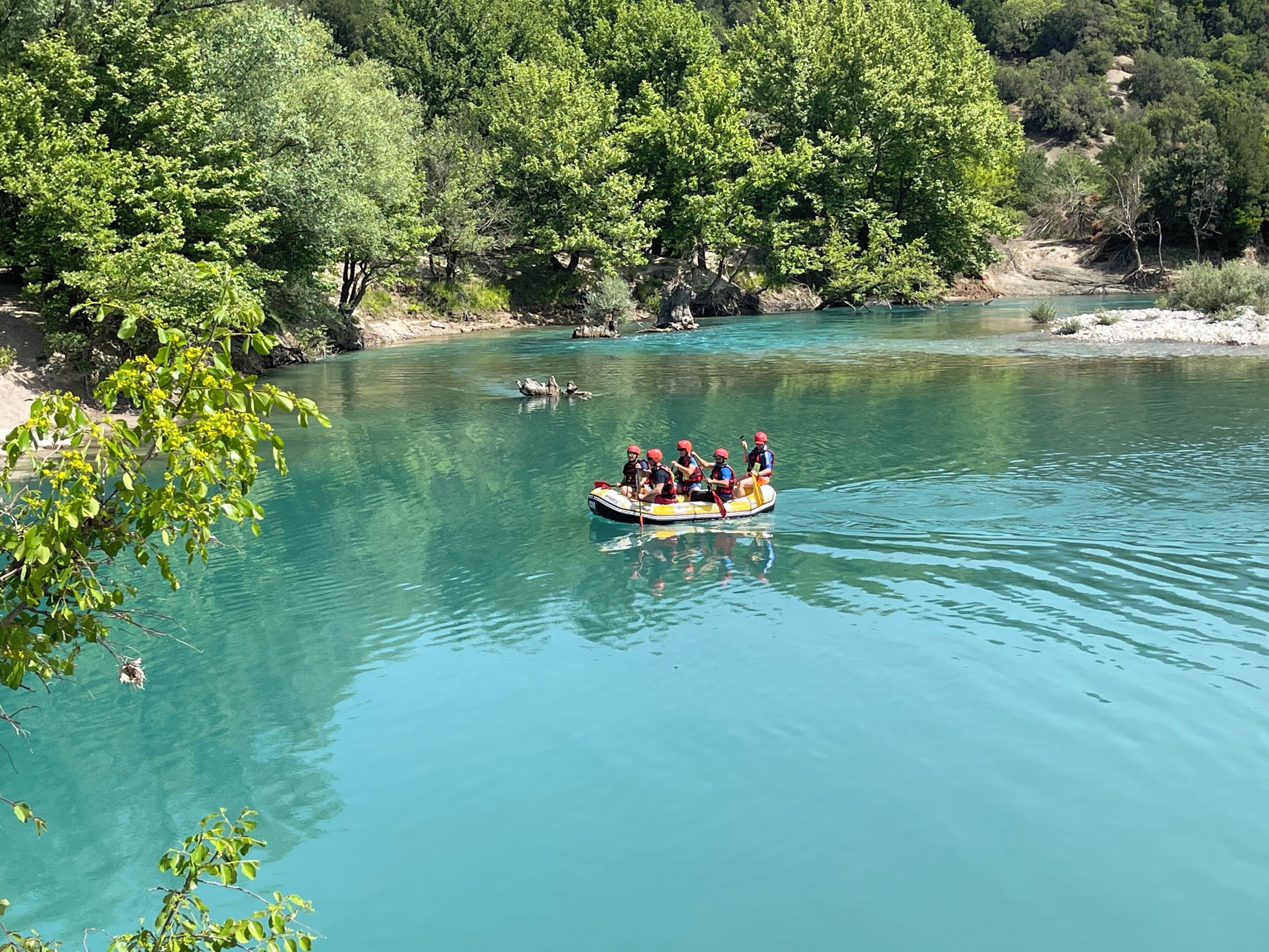 A group of people in a raft on a clear river surrounded by dense greenery.