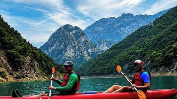 Two people kayaking on a calm lake with mountains in the background.