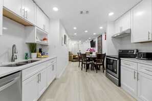 A modern kitchen with white cabinets, a dining area with a table and chairs, a built-in oven, and a microwave. - 3BR Near AT&T Stadium | Free Parking (Arlington)