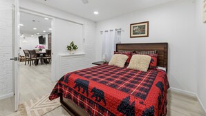A bedroom with a bed, a ceiling fan, a window with curtains, and a dining area visible through an open door. - Spacious 3BR Retreat • Sleeps 6 • Free Parking (Arlington)