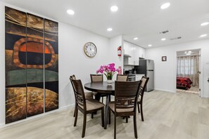 A modern dining area with a round table, chairs, a clock, and a large abstract painting. - 3BR Near AT&T Stadium | Free Parking (Arlington)