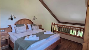 A bedroom with a wooden bed, a nightstand, a hanging light fixture, and a view of greenery through a window. - Alpine Retreat Apt: Scenic Bavarian Nature, (Fischbachau)