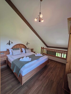 Ein Schlafzimmer mit einem hölzernen Bett, einem Nachttisch, einer Hängeleuchte und Blick auf Grün hinter einem Fenster.