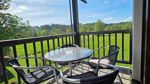 A wooden deck with a metal table and chairs, overlooking a green landscape. - Alpine Retreat Apt: Scenic Bavarian Nature, (Fischbachau)