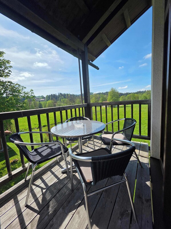 A wooden deck with a metal table and chairs, overlooking a green landscape.