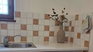 A kitchen with a sink, wooden cabinets, a tiled backsplash, and a woven vase with flowers. - Alpine Retreat Apt: Scenic Bavarian Nature, (Fischbachau)