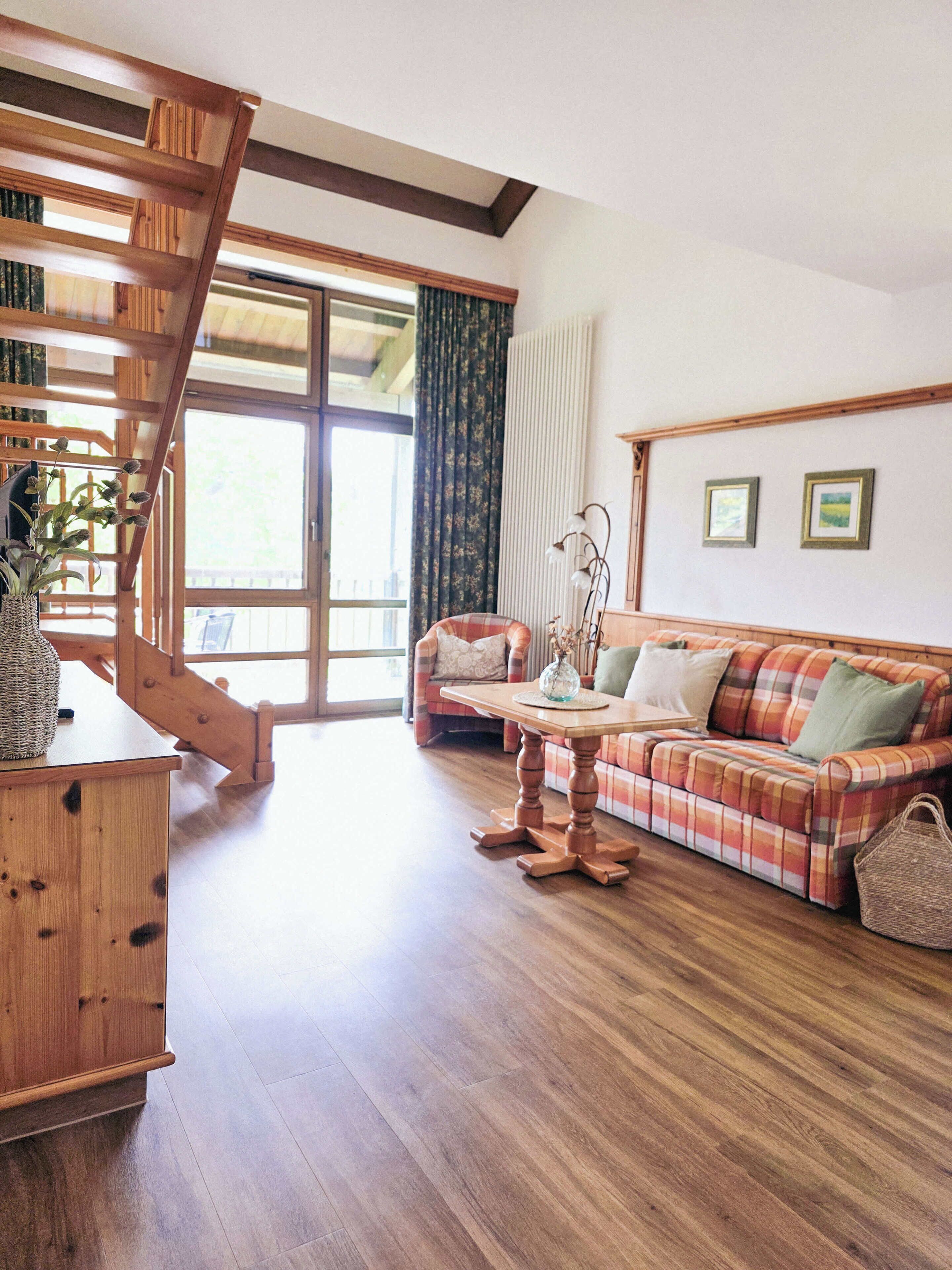 Eine Holztreppe, ein kariertes Sofa, ein Holztisch und ein Fenster mit Vorhängen.