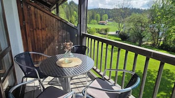 A wooden deck with a round table and chairs, a view of a green landscape, and a wooden fence.