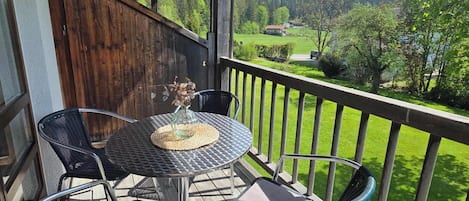 Una terraza de madera con una mesa redonda y sillas, vista a un paisaje verde y una valla de madera.