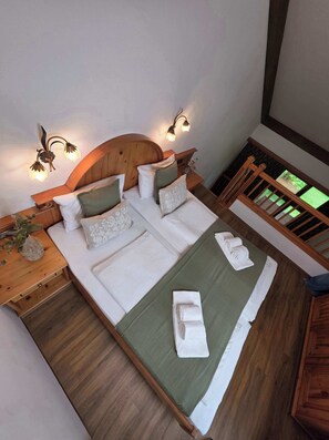 Ein Schlafzimmer mit einem Holz-Kopfteil, zwei Nachttischen mit Lampen, einem Bett mit grüner Bettwäsche und Blick ins Freie durch ein Fenster.