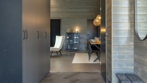 A modern interior with a dark-toned wardrobe, a white upholstered chair, a dining table set with plates and glasses, and a wooden cabinet with glass doors. - Villa Noel B (Lappi)