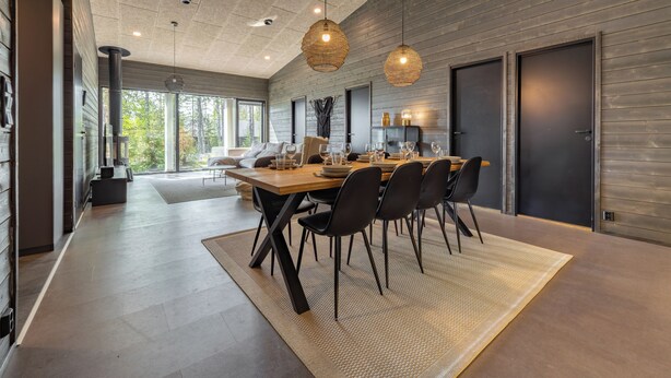 A modern dining area with a long table, black chairs, and hanging pendant lights. - Villa Noel B (Lappi)