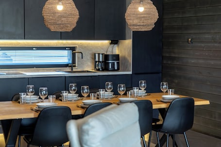 A modern kitchen with a dining table set for six, equipped with a coffee maker, a kettle, and a built-in oven.