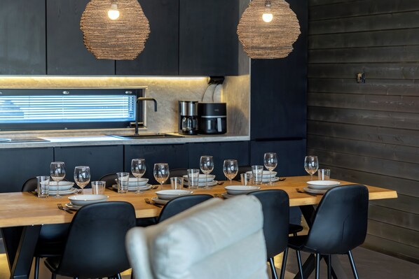 A modern kitchen with a dining table set for six, equipped with a coffee maker, a kettle, and a built-in oven.