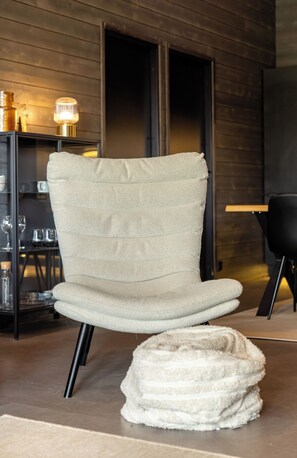 A modern chair with a high backrest and a cushioned seat, positioned in a room with wooden walls and a glass table with wine glasses. - Villa Noel B (Lappi)