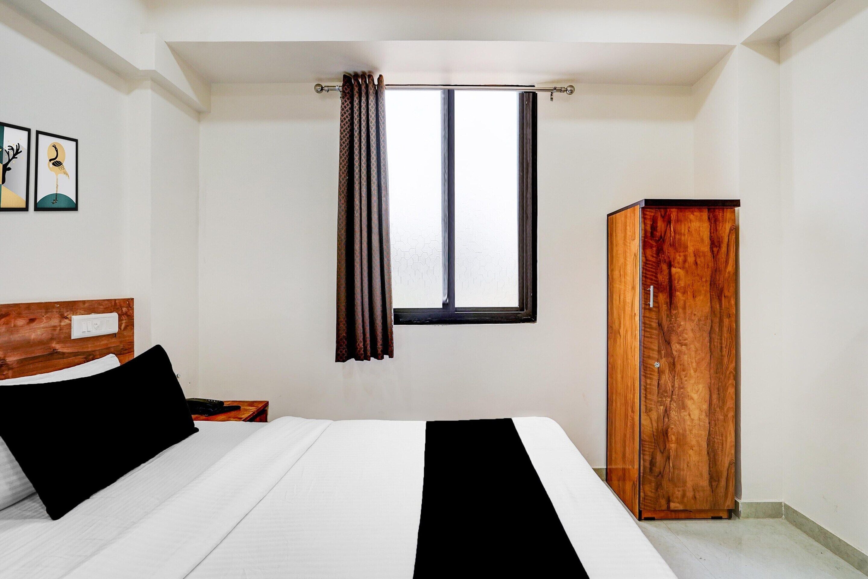 A bedroom with a bed, a wooden wardrobe, a window with curtains, and two wall-mounted artworks.