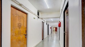 A long, narrow hallway with doors on both sides, a fire extinguisher mounted on the wall, and a ceiling with fluorescent lighting.