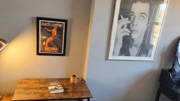 A room with a wooden chair, a black bean bag, a small table with a book and a mug, and two framed pictures on the wall.