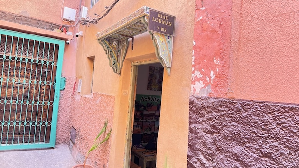 A narrow alleyway with a turquoise gate, a sign reading 'RIAD LOKMAN 7 BIS,' and a shop entrance with a poster advertising activities. - Riad Dar Lokman (Marrakech)