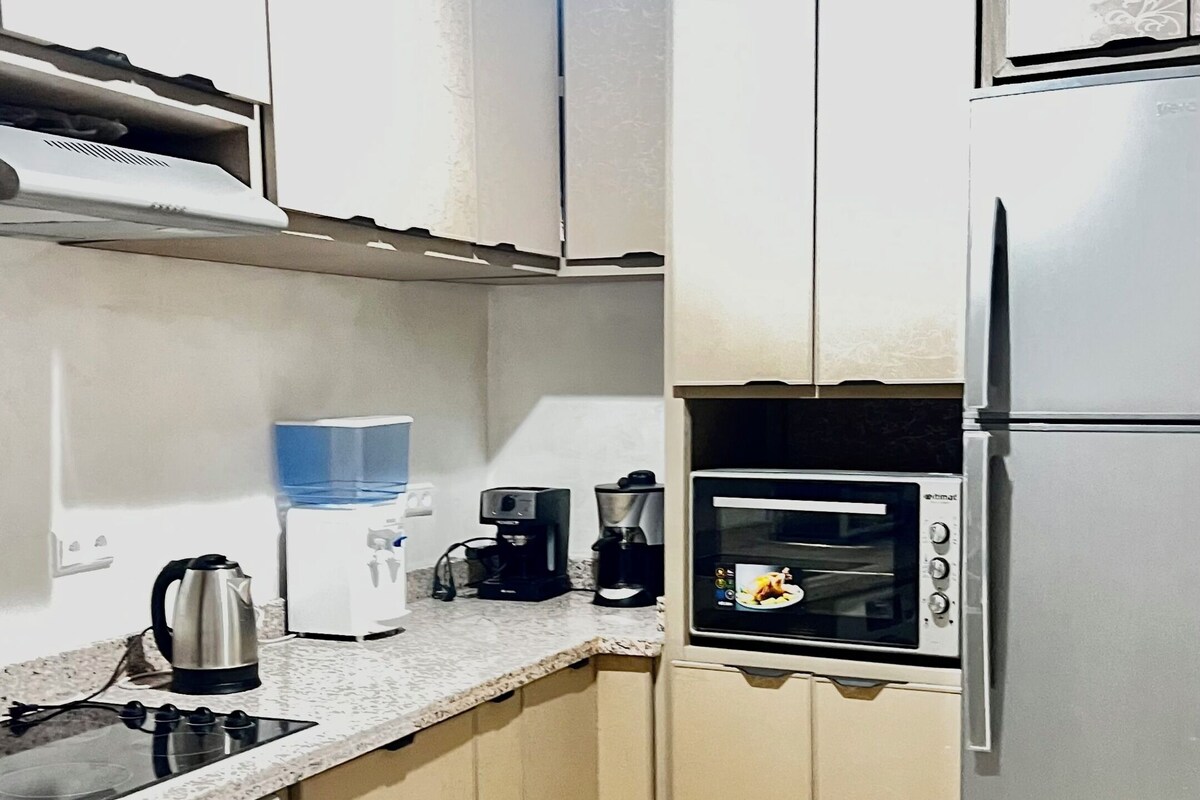 A compact kitchen with a washing machine, a coffee maker, a kettle, a microwave, and a refrigerator.