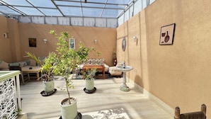 A sunlit room with a glass ceiling, a wooden table, a sofa, and potted plants. - Riad Dar Lokman (Marrakech)