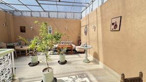 A sunlit room with a glass ceiling, a wooden table, a sofa, and potted plants. - Riad Dar Lokman (Marrakech)