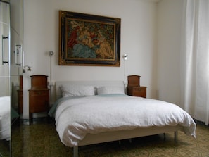 A bedroom with a bed, a nightstand, a dresser, a painting on the wall, and a patterned floor.