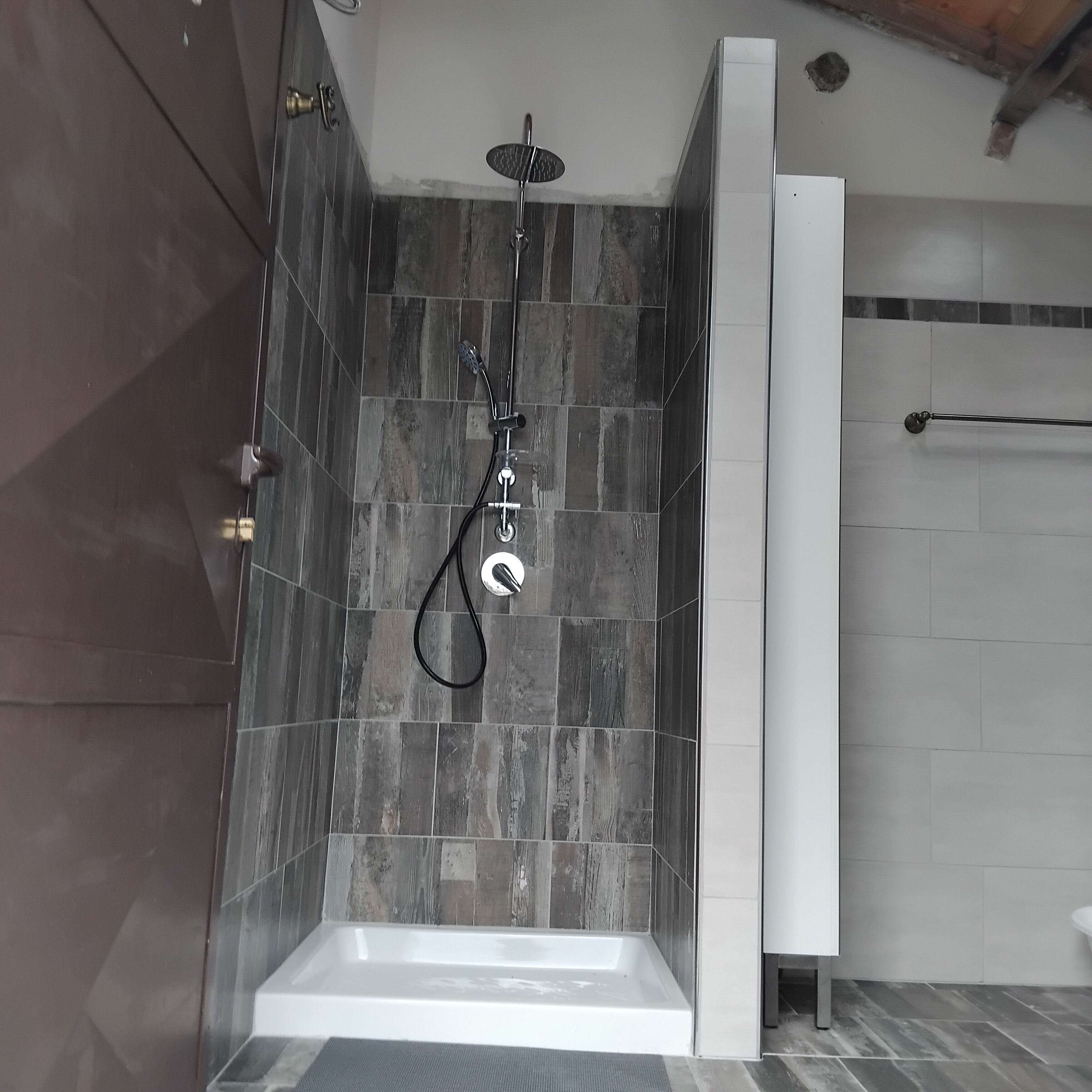 A modern shower with a handheld showerhead, a built-in seat, and a wall-mounted faucet.