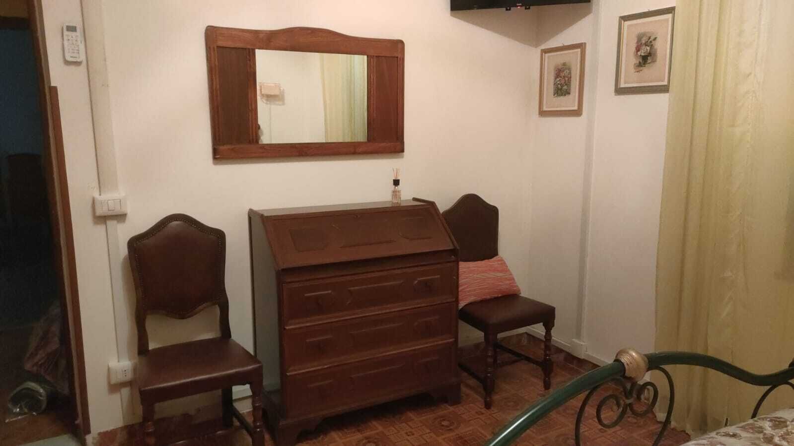 Ein Schlafzimmer mit einem hölzernen Schminktisch, zwei Stühlen, einem Spiegel und einem Bett mit grünem Metallgestell.