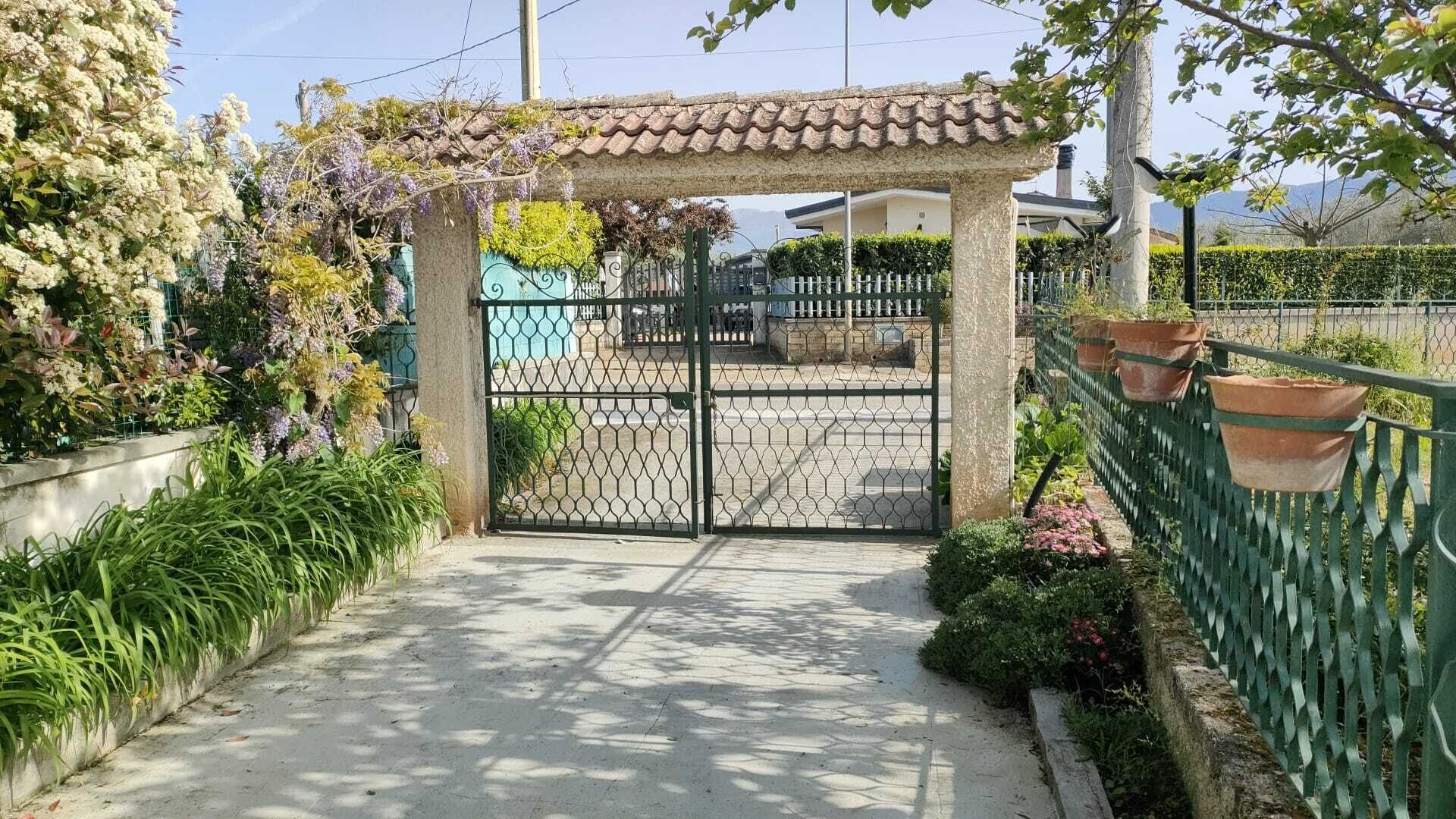 Uma entrada com portão, pérgola, caminho e cerca com vasos de plantas.
